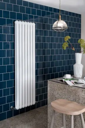 A four barred vertical radiator on a dark blue tiled wall