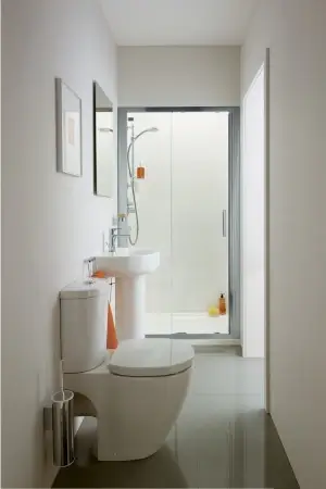 Looking beyond a white toilet, we see a white sink and glass-doored shower